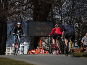 A sign warns people to social distance and keep at least 2 metres apart from one another due to concerns about the spread of the coronavirus, as ride bicycles and run on the seawall, in Vancouver, on Wednesday, March 25, 2020.