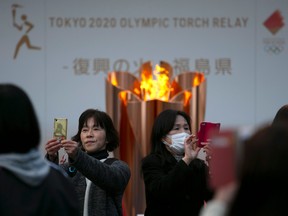 People take pictures with the Olympic Flame during a ceremony in Fukushima City, Japan, Tuesday, March 24, 2020.