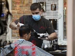 A barber wears a protective face mask as he cuts the hair of a customer in central Leeds, northern England on the morning of March 21, 2020.