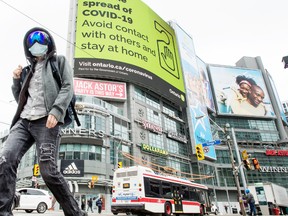 A pedestrian wearing a mask walks across Yonge Street at Dundas Street with a “Stop The Spread Of Covid 19” notice in the background during the Covid 19 pandemic, Friday April 3, 2020.