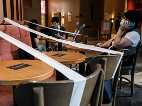 Customers wearing face masks as a precautionary measure against the COVID-19 coronavirus sit in a cafe, which has masking tape on every other table to enforce social distancing, in Hong Kong on April 21, 2020.