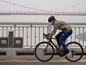 A man wearing a face mask rides a bicycle on Wuhan Bridge over the Yangtze River in Wuhan, in China's central Hubei province, on April 1, 2020, where the COVID-19 coronavirus first emerged last year but is partly reopening after more than two months of near total isolation.