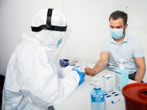 A health worker wears a protective mask and suit as she extracts blood from a patient to perform an antibody test for COVID-19 in Krakow, Poland, on April 9.