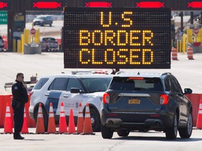 In this file photo U.S. Customs officers speak with people in a car beside a sign saying that the U.S. border is closed at the U.S./Canada border in Lansdowne, Ontario, on March 22, 2020.