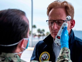 This U.S. Navy handout photo released March 31, 2020 shows  Acting Secretary of the Navy Thomas B. Modly having his temperature read as part of a COVID-19 screening prior to a tour of the Military Sealift Command hospital ship USNS Mercy (T-AH 19) and the Los Angeles World Cruise Center, March 31, 2020.