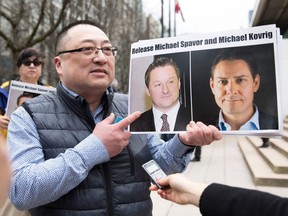In this file photo taken on March 6, 2019, Louis Huang of Vancouver Freedom and Democracy for China holds photos of Canadians Michael Spavor and Michael Kovrig, who are being detained by China, outside British Columbia Supreme Court, in Vancouver.