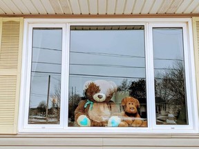 A toy bear and another stuffie sits in a window, waiting for the neighbourhood kids to notice them.