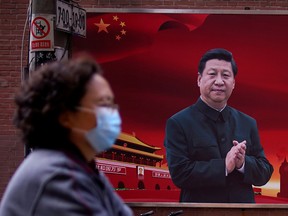 A woman wearing a protective mask walks past a portrait of Chinese President Xi Jinping in Shanghai.