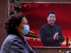 A woman wearing a protective mask rides past a portrait of Chinese President Xi Jinping, in Shanghai on March 12.