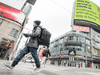A pedestrian walks across Toronto’s Yonge Street and Dundas Street intersection, as a nearby billboard urges people to “Stop The Spread Of COVID-19.”