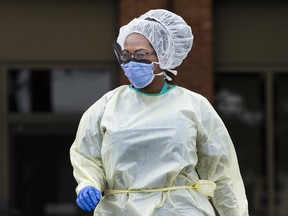 A health care worker wearing protective gear walks between a COVID-19 assessment centre at The Scarborough Hospital in Scarborough, Ont., on Friday, April 3, 2020.