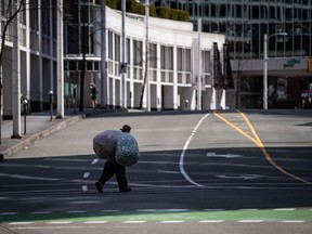 A man carrying bags of bottles and cans walks across an empty street near the waterfront in downtown Vancouver, on Sunday, March 29, 2020. Researchers, epidemiologists and advocates are calling for better data on who is getting and dying from COVID-19 to make sure no minority or socioeconomic group is unduly impacted.