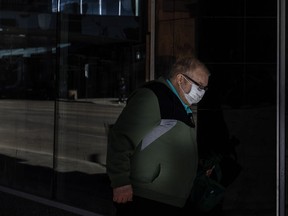 A person walks through a spot of light while wearing a mask to help the stop of COVID-19 during the global pandemic, in Edmonton on Wednesday, April 8, 2020.