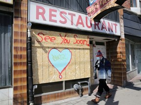 A man wearing a protective face mask passes a boarded up restaurant during the global COVID-19 outbreak, in Toronto, April 6, 2020.