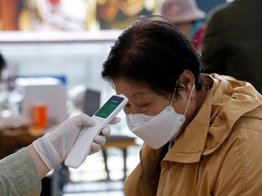 A woman wearing a preventive face mask has her temperature checked, as a safety measure to prevent the further spread of the coronavirus, before casting a ballot for parliamentary elections at a polling station in Seoul, South Korea, April 10, 2020.