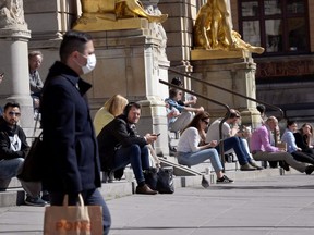 A man wearing a protective face mask walks near to people sitting at the stairs of the Royal Dramatic Theater  in Stockholm, Sweden April 22, 2020.