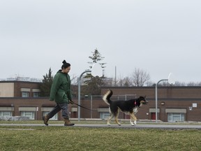 A woman walks her dog past removed basketball nets at the closed Tomken Road Middle School in Mississauga, Ont.
