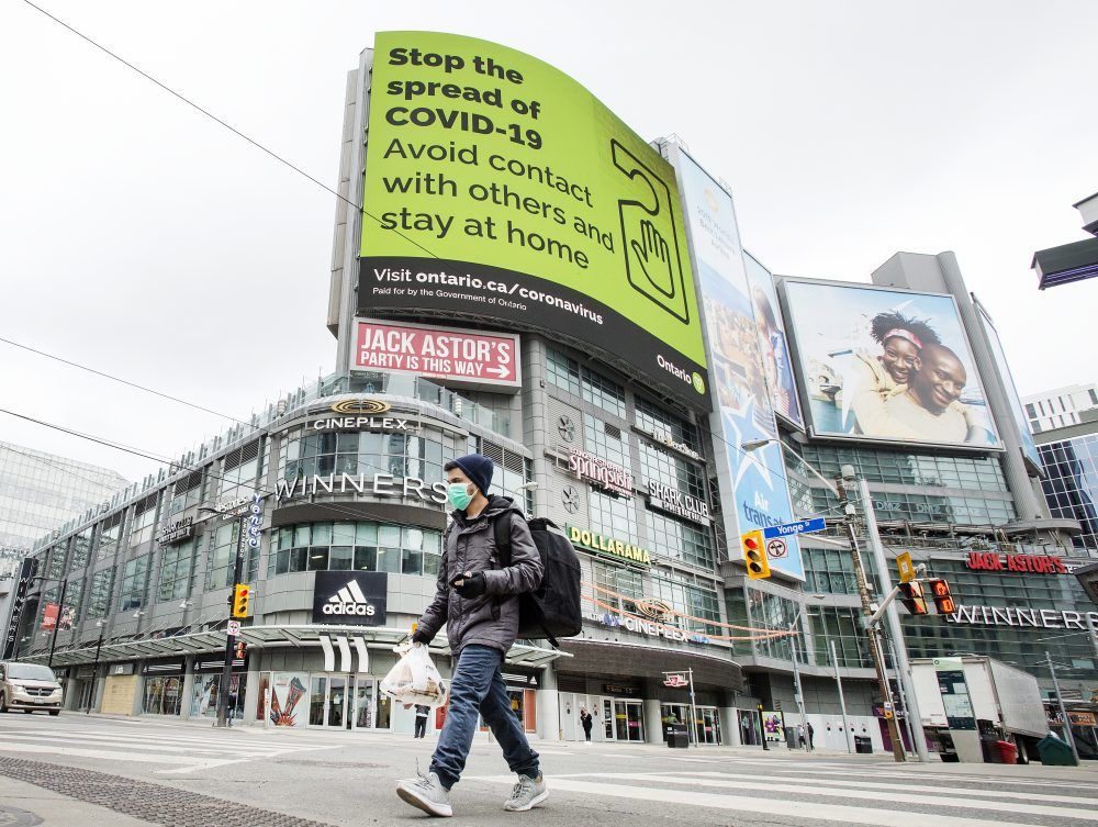  a pedestrian wearing a mask walks across yonge street at dundas street with a “stop the spread of covid 19” notice in the background, april 3, 2020.
