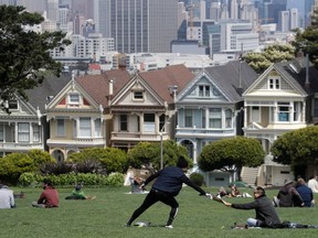 A man reaches to grab something as he maintains distance from another man at Alamo Square Park in San Francisco, Sunday, April 26, 2020, during the coronavirus outbreak.