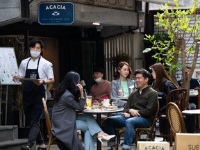 People wearing protective masks sit outside a cafe in the Garosu-gil neighborhood of the Gangnam district of Seoul, South Korea, on Saturday, April 18, 2020.
