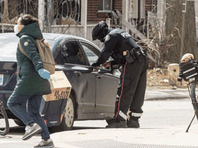 Police give a ticket to a vehicle driver as a woman in a mask walks by in Toronto during the COVID-19 pandemic.