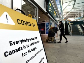 A traveller walks past signage in Vancouver International Airport (YVR) asking international travellers to self-isolate for 14 days. Starting Friday, the request will be enforced in B.C.
