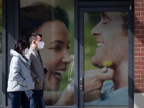 People wearing protective face masks walk past a photograph outside a drug store, in Vancouver, on Sunday, April 5, 2020.