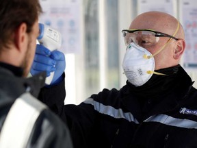 An employee, wearing a protective face mask, checks the temperature of a colleague at the entrance of a Michelin tyre's factory.