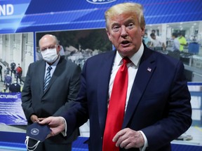 U.S. President Donald Trump holds a protective face mask with a presidential seal on it that he said he had been wearing earlier in his tour as Ford Motor Company CEO Jim Hackett looks on at the Ford Rawsonville Components Plant that is manufacturing ventilators, masks and other medical supplies during the coronavirus disease (COVID-19) pandemic in Ypsilanti, Michigan, U.S., May 21, 2020.