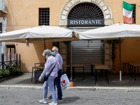 Pedestrians wearing protective face masks pass closed restaurants in Rome, Italy, on Tuesday, May 19, 2020.