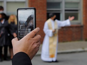 A parishioner provides a live stream for remote mourners as Father Hilario Sanez performs funeral blessings for Jose Agustin Iraheta, who died from the coronavirus disease (COVID-19), outside Saint Rose of Lima Catholic Church in Chelsea, Massachusetts, U.S., May 12, 2020.