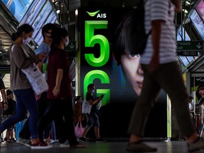 Commuters walk in front of a 5G advertisement at a train station in Bangkok on May 5, 2020. The 5G telecommunication technology has found itself in the middle of conspiracy theories related to the spread of COVID-19.