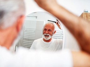 Smiling senior man brushing his hair in the bathroom.