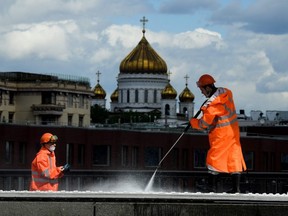 Municipal workers wearing face masks clean Krymsky Bridge across the Moskva river, with the Cathedral of Christ the Saviour seen in the background, in downtown Moscow on May 20, 2020, amid the COVID-19 coronavirus pandemic.