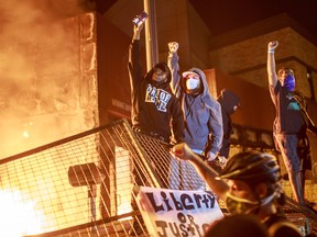 Protesters hold up their fists as flames rise behind them in front of the Third Police Precinct in Minnneapolis on May 28.