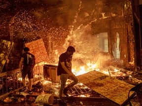 Protesters walk past burning debris outside the Third Police Precinct on May 28, 2020 in Minneapolis, Minnesota, during a protest over the death of George Floyd, an unarmed black man, who died after a police officer kneeled on his neck for several minutes.