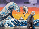 A pedestrian wearing a mask walks past a mural of a wave by artist Kinka Izakaya in Toronto as concerns that a second wave of COVID-19 may occur as restrictions on communities are eased.