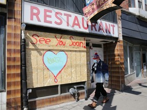 A man wearing a protective face mask passes a boarded up restaurant in Toronto,  April 6, 2020.