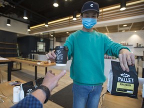 A server wears a protective face mask as he passes a coffee to a customer in Vancouver, Wednesday, May 20, 2020. British Columbia has entered into phase 2 of the provinces re-start plan allowing some business to reopen.