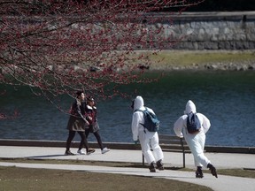 Two people wearing personal protective equipment, including respirators and coverall suits in-line skate on the seawall at Stanley Park in Vancouver on Sunday, April 5, 2020.