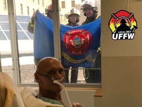 Rick Sterzer, a 65-year-old retired firefighter, sits in his hospital bed as Winnipeg firefighters stand outside his window in this handout photo which was posted to the United Fire Fighters of Winnipeg Local 867 on April 11, 2020.