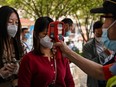 A worker wearing a face mask checks passengers body temperatures and a health code on their phones before they take a taxi after arriving at Hankou railway station in Wuhan, Hubei Province on May 12, 2020.