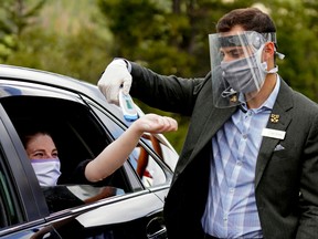 A woman gets her temperature checked by Fairmont Jasper Park Lodge employee Naji Khouri before being allowed entrance onto the grounds of the hotel in Jasper National Park on June 4, 2020.
