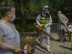 A Chinese member of Blue Sky Rescue wears a protective suit as he walks by residents while fumigating to prevent COVID-19 at a residential compound on June 21, 2020 in Beijing, China.