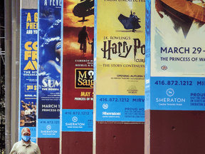 A man in Toronto walks by theatre posters for shows that have been either postponed or cancelled.