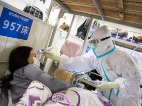 This photo taken on February 17, 2020 shows a member of the medical staff checking the body temperature of a patient who has displayed mild symptoms of the COVID-19 coronavirus, at an exhibition centre converted into a hospital in Wuhan in China's central Hubei province.