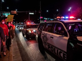 A police officer looks out the car window as people march, on June 1, 2020, in downtown Las Vegas, while taking part in a Black Lives Matter rally in response to the recent death of George Floyd, an unarmed black man who died while in police custody.  Thousands of National Guard troops patrolled major US cities after five consecutive nights of protests over racism and police brutality that boiled over into arson and looting, sending shock waves through the country.