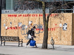 A woman wearing a mask walks past a shuttered business on Toronto's Queen Street West during the COVID-19 pandemic.