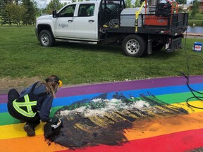 A city worker cleans a rainbow pathway in Airdrie, Alberta on Saturday June 27, 2020. A Pride organization north of Calgary says it will paint over vandalism to its rainbow pathway as many times as necessary following the latest incident where the path appears to have been tarred-and-feathered.