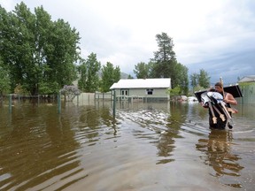 Resident Lars Androsoff carries his friend's guitars as he walks through the floodwaters in Grand Forks, B.C., on Thursday, May 17, 2018. A flood warning has been posted for a section of southwestern British Columbia as weekend rains and snowmelt combined to swell many rivers across the region.